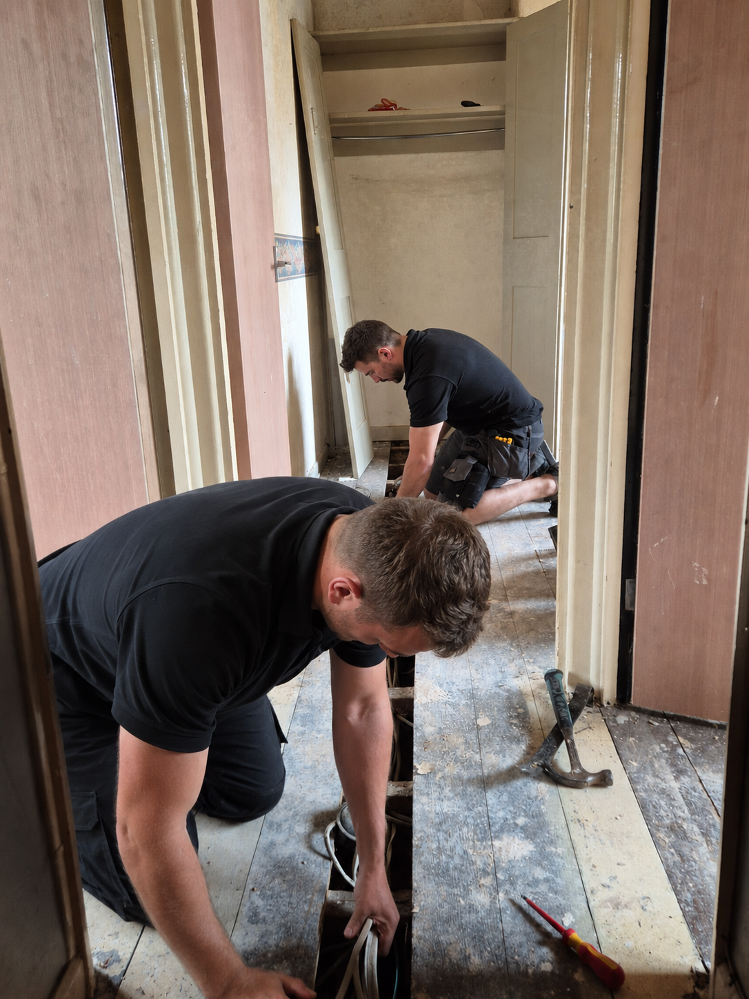 Electricians running cable beneath floorboards